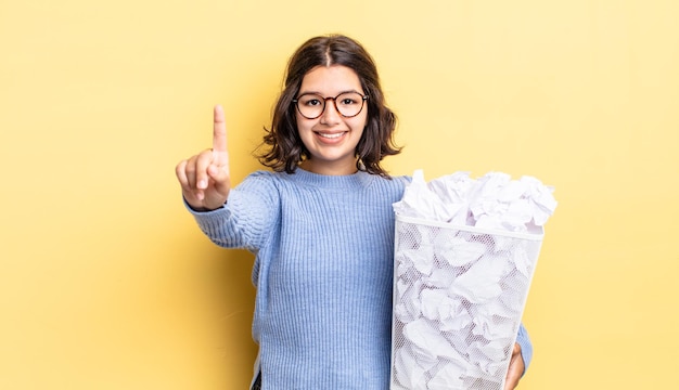 Junge hispanische Frau, die lächelt und freundlich aussieht und das Konzept Nummer eins für Fail-Trash zeigt