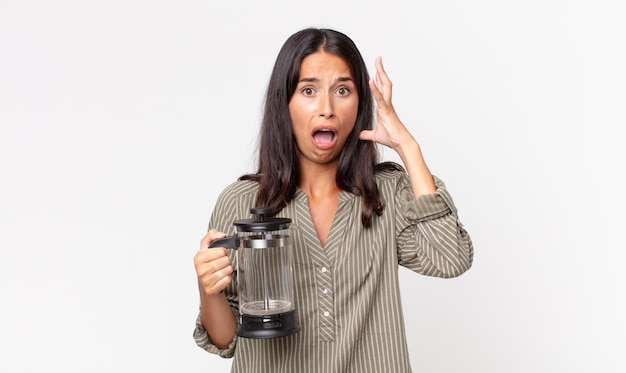 Junge hispanische Frau, die mit den Händen in die Luft schreit und eine manuelle Kaffeemaschine hält