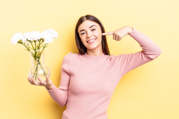 Junge hispanische Frau, die selbstbewusst lächelt und auf ein breites Lächeln zeigt. Blumentopfkonzept