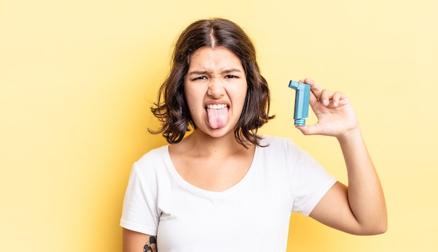 Junge hispanische Frau, die sich angewidert und gereizt fühlt und die Zunge herausstreckt. Asthma-Konzept