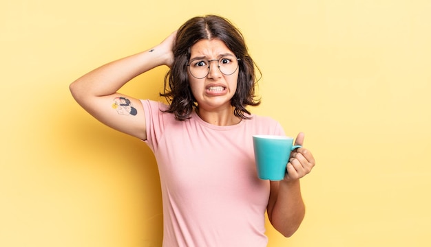 Foto junge hispanische frau, die sich gestresst, ängstlich oder verängstigt fühlt, mit den händen auf dem kopf. kaffeebecher-konzept