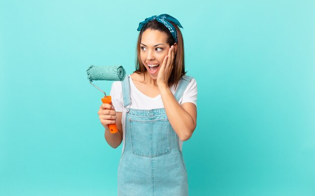 Junge hispanische Frau, die sich glücklich, aufgeregt und überrascht fühlt und eine Wand malt