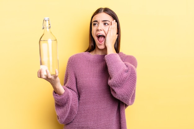 Junge hispanische Frau, die sich glücklich, aufgeregt und überrascht fühlt. Wasserflaschenkonzept