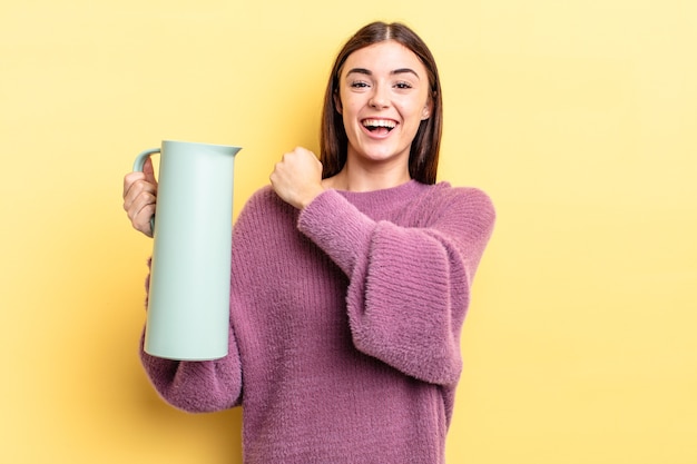 Junge hispanische Frau, die sich glücklich fühlt und einer Herausforderung gegenübersteht oder feiert. Kaffee-Thermos-Konzept