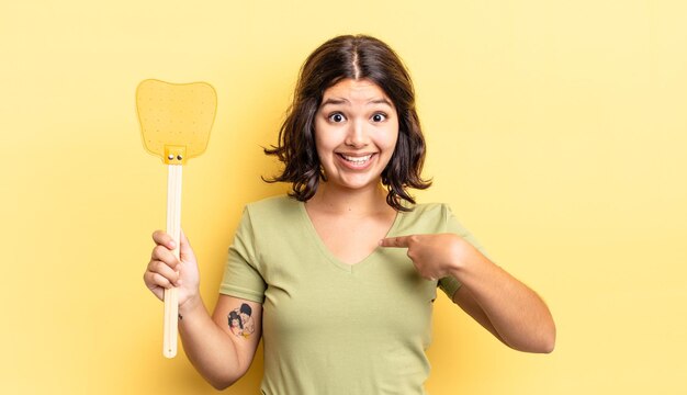 Junge hispanische Frau, die sich glücklich fühlt und mit einem aufgeregten auf sich selbst zeigt. Fliegen töten Konzept