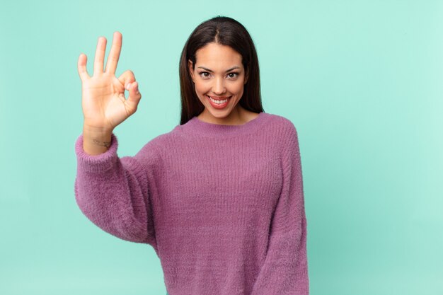 Junge hispanische Frau, die sich glücklich fühlt und Zustimmung mit einer okayen Geste zeigt