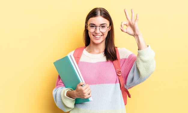 Junge hispanische Frau, die sich glücklich fühlt und Zustimmung mit okayer Geste zeigt. studentisches Konzept