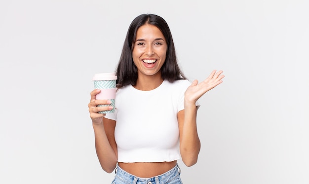 Junge hispanische Frau, die sich glücklich und erstaunt über etwas Unglaubliches fühlt und einen Kaffeebehälter zum Mitnehmen hält