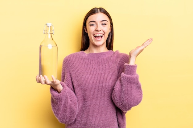 Junge hispanische Frau, die sich glücklich und erstaunt über etwas Unglaubliches fühlt. Wasserflaschenkonzept