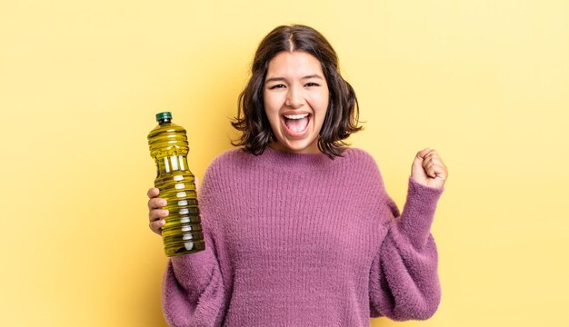 Junge hispanische Frau, die sich schockiert fühlt, lacht und den Erfolg feiert. Olivenöl Konzept