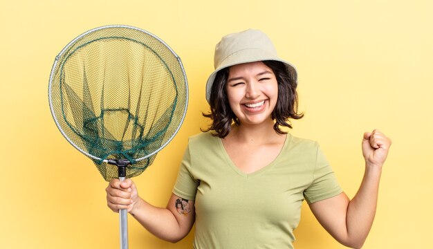 Junge hispanische Frau, die sich schockiert fühlt, lacht und Erfolg feiert. Fischernetzkonzept