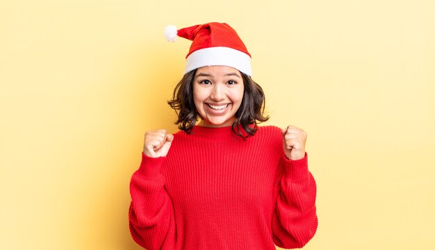 Junge hispanische Frau, die sich schockiert fühlt, lacht und Erfolg feiert. Weihnachtskonzept