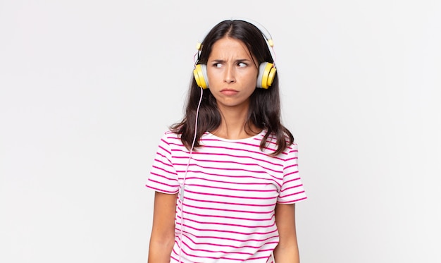 Junge hispanische Frau, die sich traurig, verärgert oder wütend fühlt und zur Seite schaut und Musik mit Kopfhörern hört