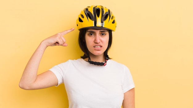 Junge hispanische Frau, die sich verwirrt und verwirrt fühlt und zeigt, dass Sie ein verrücktes Fahrradhelm-Konzept sind