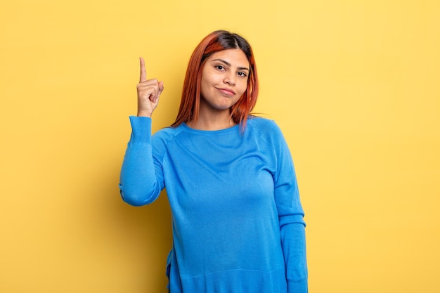 Junge hispanische Frau, die sich wie ein Genie fühlt, hält den Finger stolz in die Luft, nachdem sie eine großartige Idee realisiert hat, und sagt Heureka