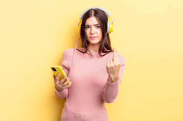 Junge hispanische Frau, die sich wütend, verärgert, rebellisch und aggressiv fühlt. Kopfhörer- und Telefonkonzept