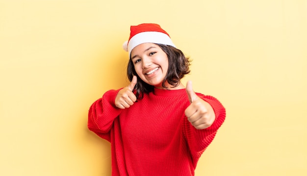 Junge hispanische Frau, die stolz ist und positiv mit Daumen nach oben lächelt. Weihnachtskonzept