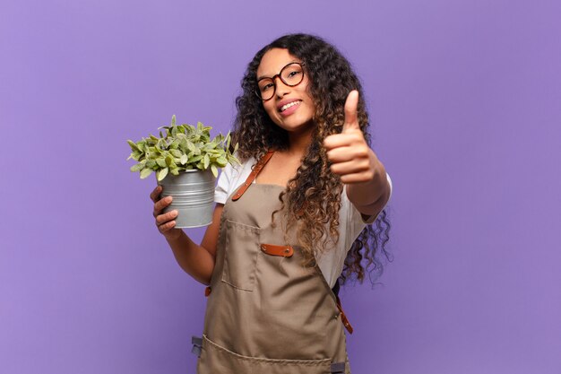 Junge hispanische Frau, die stolz, sorglos, selbstbewusst und glücklich fühlt und positiv mit Daumen hoch lächelt. Gartenwächter-Konzept