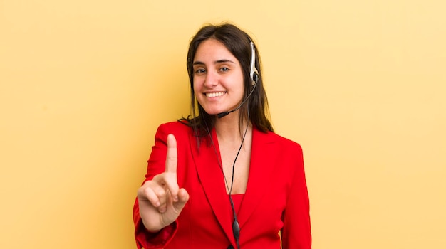 Junge hispanische Frau, die stolz und selbstbewusst lächelt und das Telemarketer-Konzept Nummer eins macht