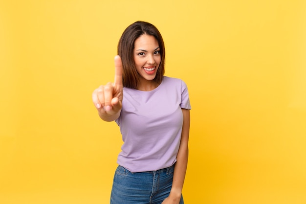 Junge hispanische Frau, die stolz und selbstbewusst lächelt und die Nummer eins macht