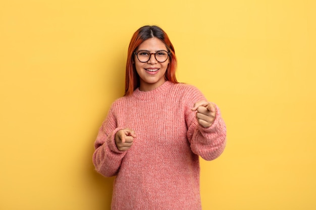 Junge hispanische Frau fühlt sich glücklich, cool, zufrieden, entspannt und erfolgreich, zeigt auf die Kamera und wählt Sie aus