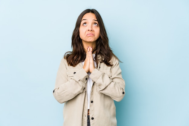 Junge hispanische Frau gemischter Abstammung isoliert Händchen haltend im Gebet nahe Mund, fühlt sich zuversichtlich.