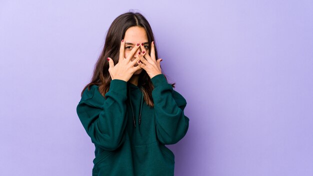 Junge hispanische Frau gemischter Rasse isolierte Blinzeln durch Finger, verlegenes bedeckendes Gesicht.