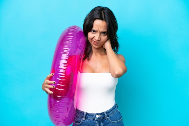 Junge hispanische Frau hält eine Luftmatratze Donut isoliert auf blauem Hintergrund mit Zweifeln