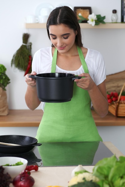 Junge hispanische Frau in einer grünen Schürze, die in der Küche kocht Hausfrau fand ein neues Rezept für ihre Suppe