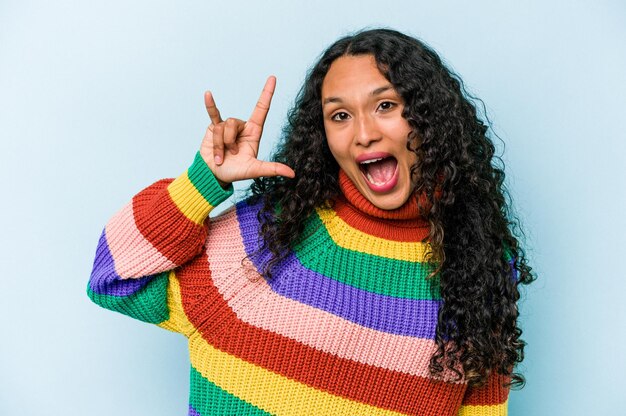 Junge hispanische Frau isoliert auf blauem Hintergrund, die eine Hörnergeste als Revolutionskonzept zeigt