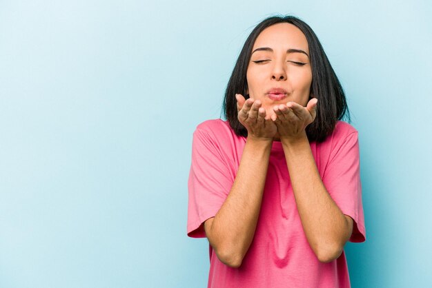 Junge hispanische Frau isoliert auf blauem Hintergrund, die Lippen faltet und Handflächen hält, um einen Luftkuss zu senden