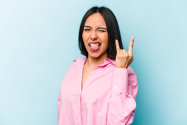 Junge hispanische Frau isoliert auf blauem Hintergrund, die Rockgeste mit den Fingern zeigt