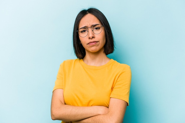 Junge hispanische Frau, isoliert auf blauem Hintergrund, verdächtig, unsicher, Sie zu untersuchen