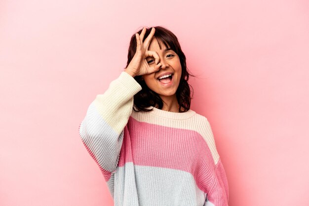 Junge hispanische Frau, isoliert auf rosa Hintergrund, aufgeregt, OK-Geste im Auge zu behalten