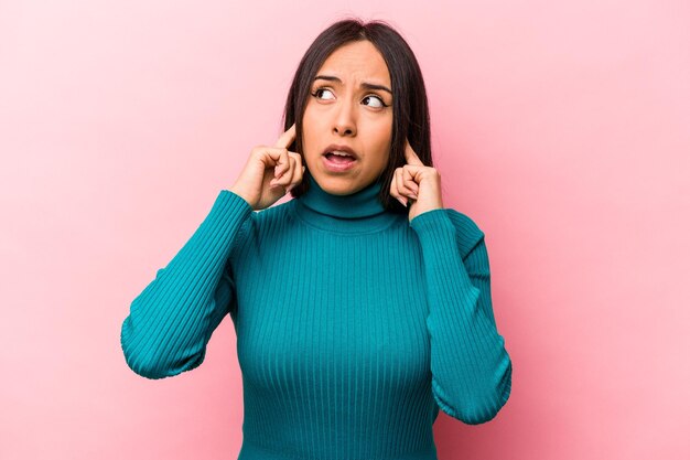 Junge hispanische Frau isoliert auf rosafarbenem Hintergrund, die Ohren mit Fingern bedeckt, gestresst und verzweifelt durch eine laute Umgebung