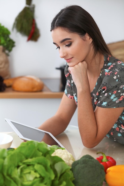 Junge hispanische Frau macht Online-Shopping per Tablet-Computer und Kreditkarte Hausfrau fand neues Rezept zum Kochen in einer Küche