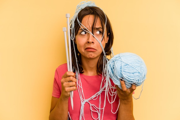 Foto junge hispanische frau mit einem wollknäuel isoliert auf gelbem hintergrund