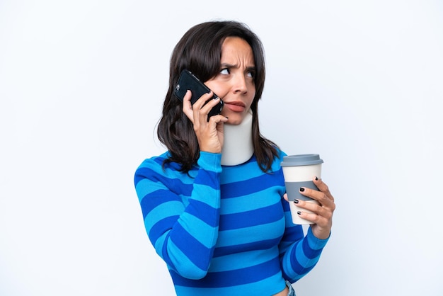 Junge hispanische Frau mit Halskrause isoliert auf weißem Hintergrund mit Kaffee zum Mitnehmen und einem Handy