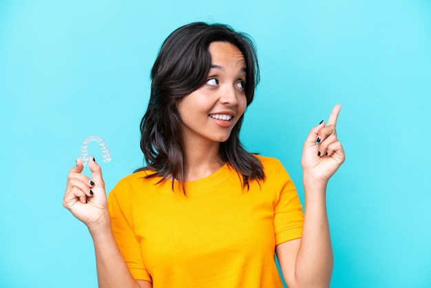 Junge hispanische Frau mit unsichtbaren Zahnspangen isoliert auf blauem Hintergrund, die auf eine großartige Idee zeigt