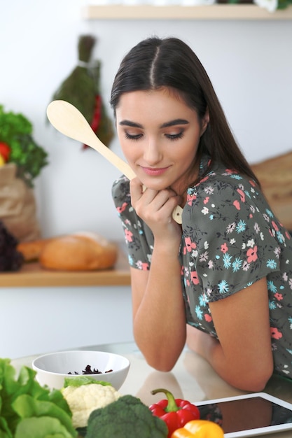 Junge hispanische frau oder studentin, die in der küche kocht mädchen mit tablet, um online einzukaufen oder ein neues rezept zu finden