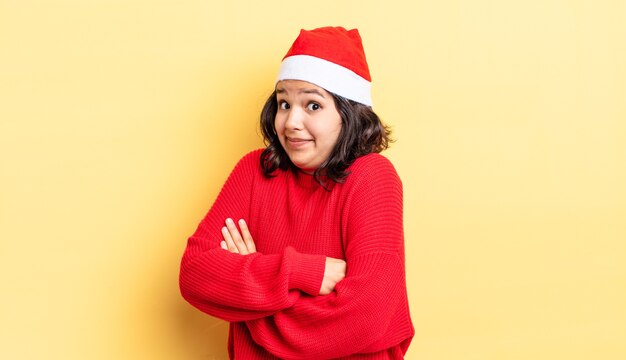 Junge hispanische Frau zuckt mit den Schultern, fühlt sich verwirrt und unsicher. Weihnachtskonzept