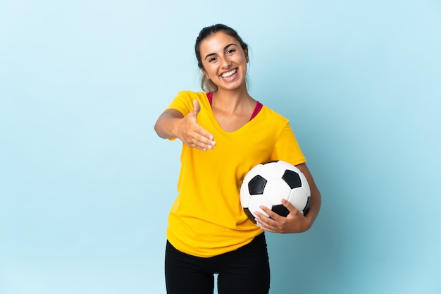 Junge hispanische Fußballspielerin Frau über isoliert auf blauen Händeschütteln für das Schließen eines guten Geschäfts