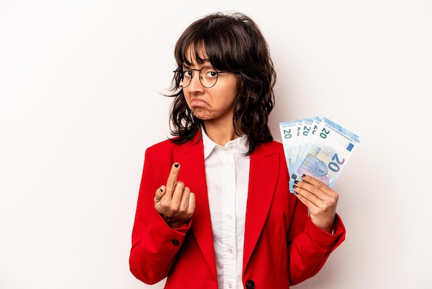 Junge hispanische Geschäftsfrau, die Banknoten isoliert auf weißem Hintergrund hält und mit dem Finger auf Sie zeigt, als würde sie einladen, näher zu kommen