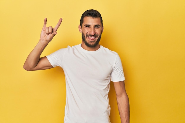 Junge hispanische Mann auf gelben Hintergrund zeigt eine Hörner-Geste als Revolutionskonzept