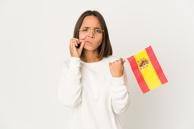 Junge hispanische Mischlingsfrau, die eine spanische Flagge mit den Fingern auf den Lippen hält, die ein Geheimnis halten.