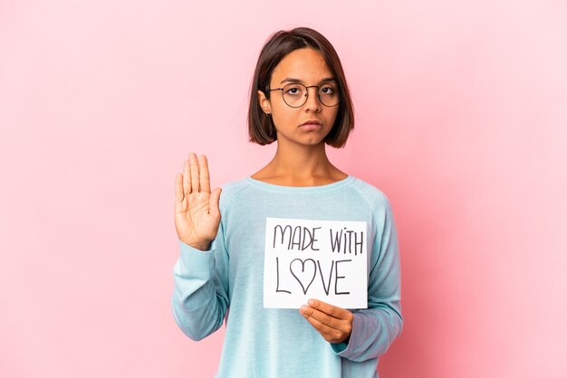 Junge hispanische Mischrassenfrau, die ein mit Liebe gemachtes Papierplakat hält, das mit ausgestreckter Hand steht und Stoppschild zeigt, das Sie verhindert.