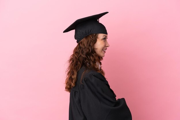 Junge Hochschulabsolventin isoliert auf rosa Hintergrund in Seitenlage