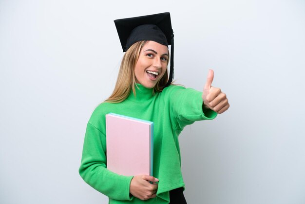 Junge Hochschulabsolventin isoliert auf weißem Hintergrund mit Daumen nach oben, weil etwas Gutes passiert ist