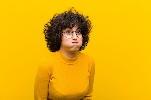 Junge hübsche afro-frau mit einem albernen, verrückten, überraschten ausdruck, puffenden wangen, sich gestopft, fett und voller essen