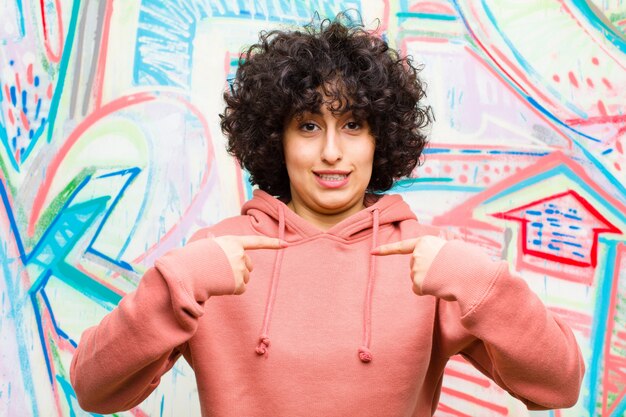 Foto junge hübsche afrofrau, die glücklich, überrascht und stolz sich fühlt und auf selbst mit einem aufgeregten, überraschten blick gegen graffitiwand zeigt